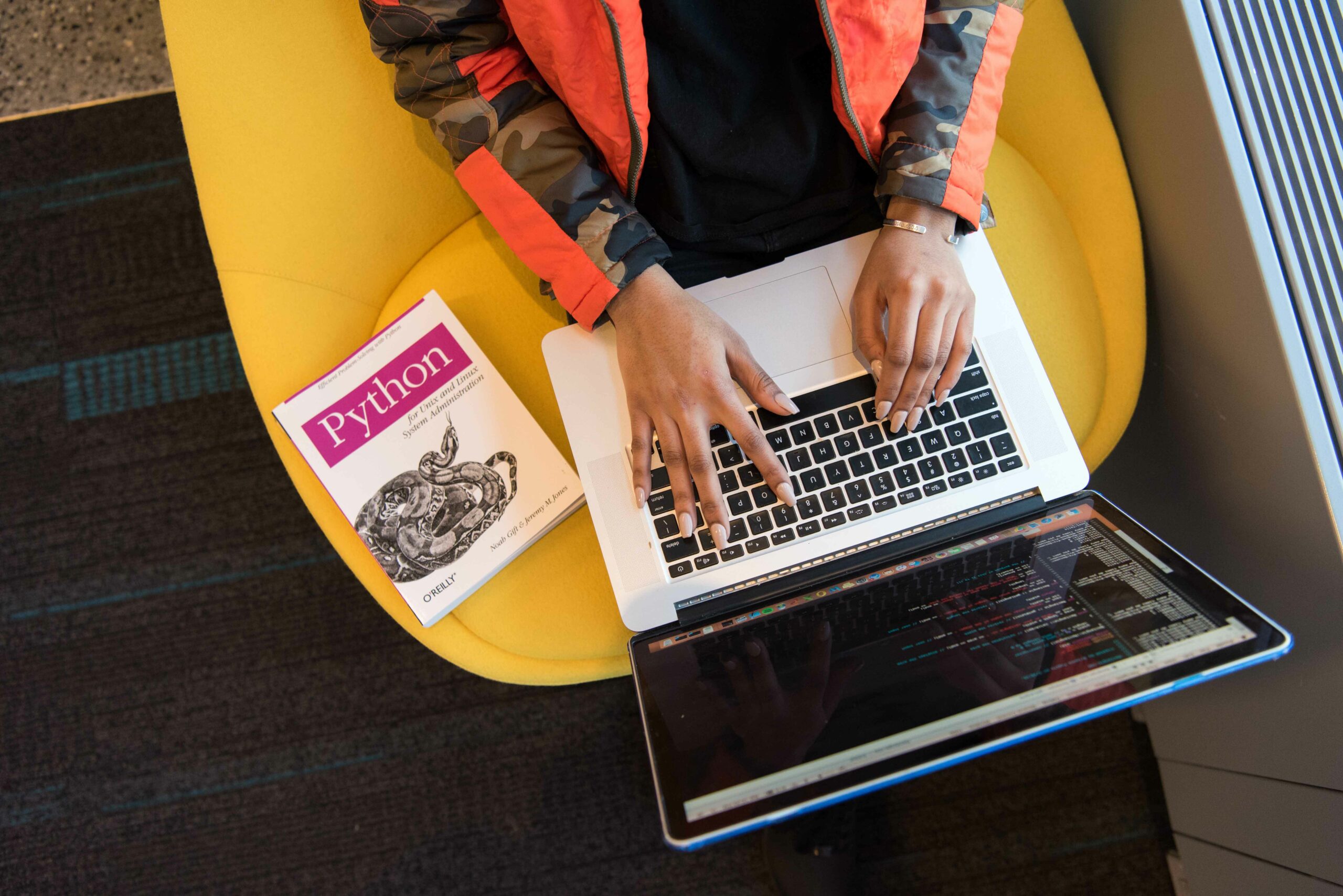 stock image of a woman typing on computer with python coding book